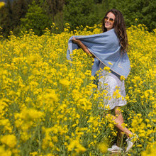 Lade das Bild in den Galerie-Viewer, Mädchen mit braunen langen Haaren dreht sich im Rapsfeld und trägt ein hellblaues Merinowolltuch mit hellgrauer Einfassung